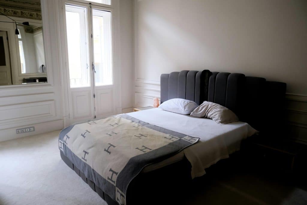 Elegant minimalist bedroom featuring a bed, double doors, and a large mirror, creating a serene indoor environment.